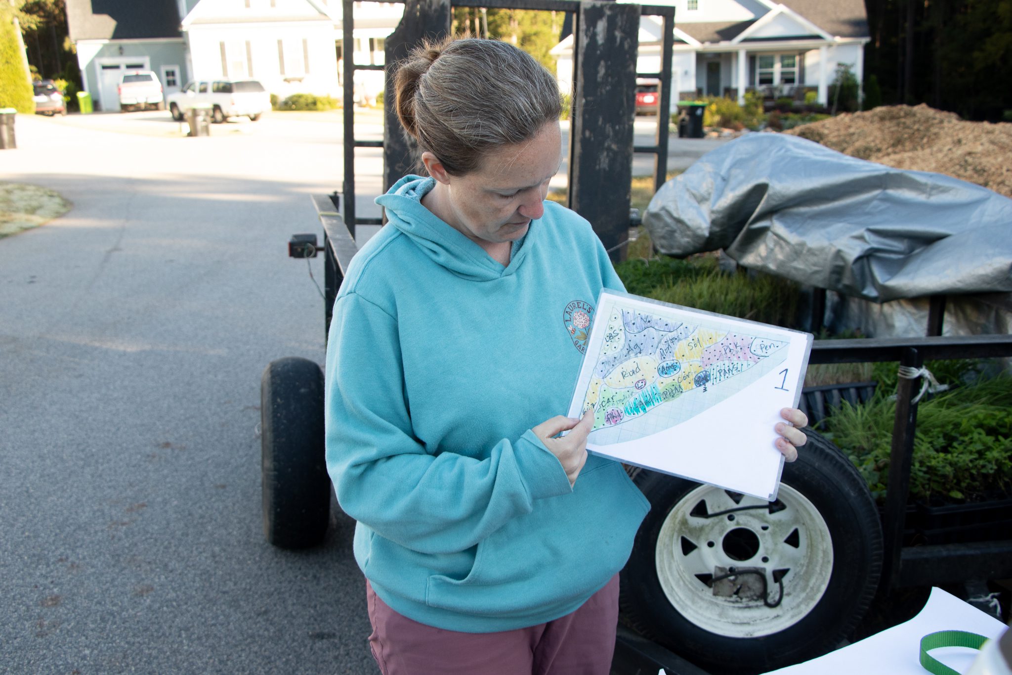 Woman in turquoise hoodie reading a colorful booklet outdoors.